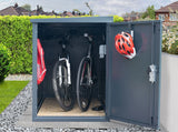 Bicycle storage shed with two bicycles and a helmet on a residential street.